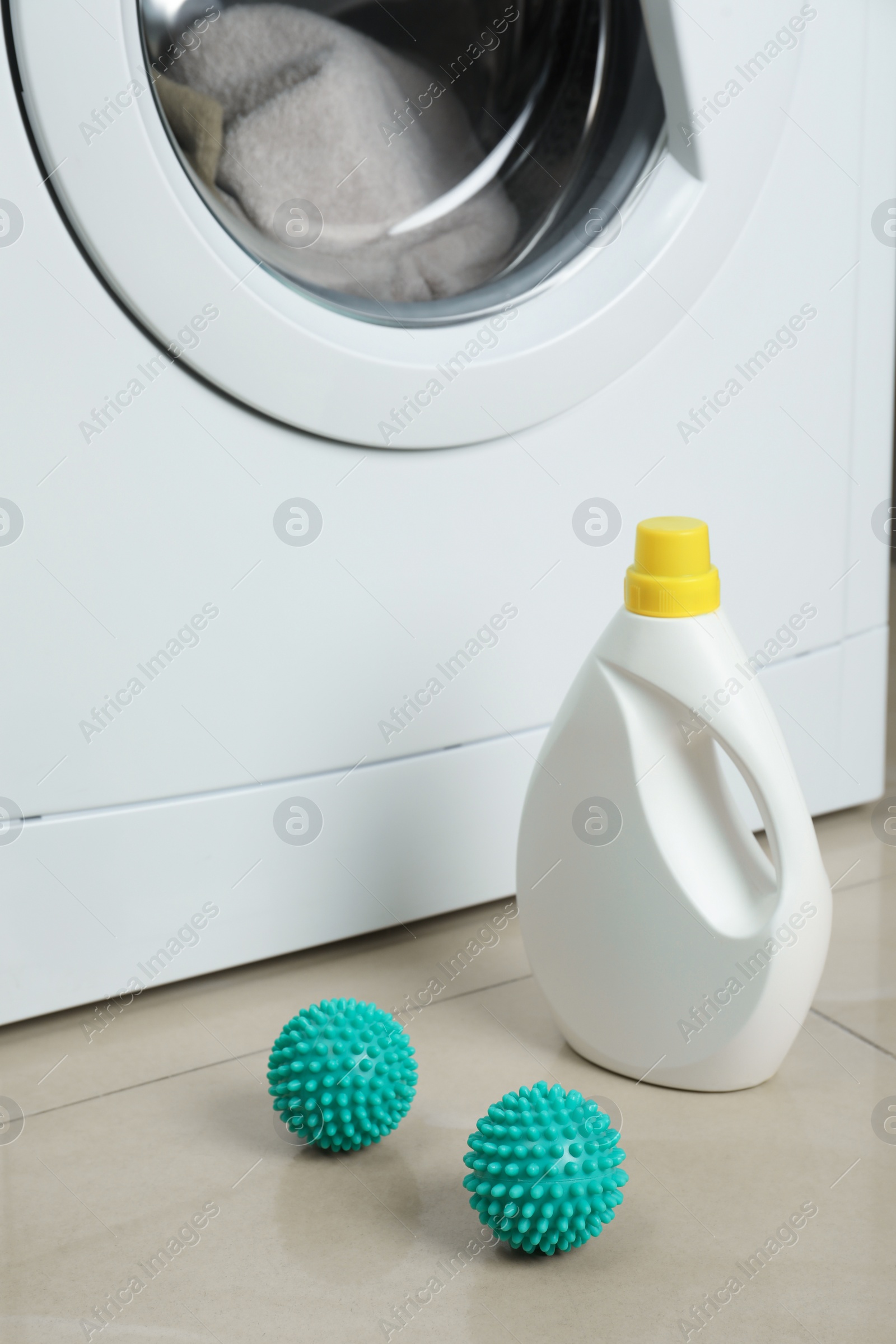 Photo of Laundry detergent and dryer balls near washing machine on floor