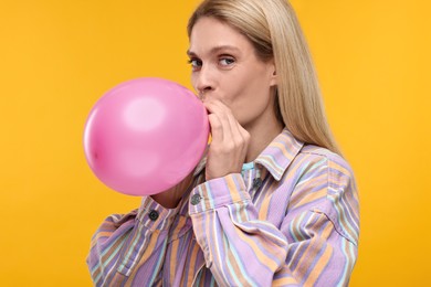 Woman blowing up balloon on yellow background
