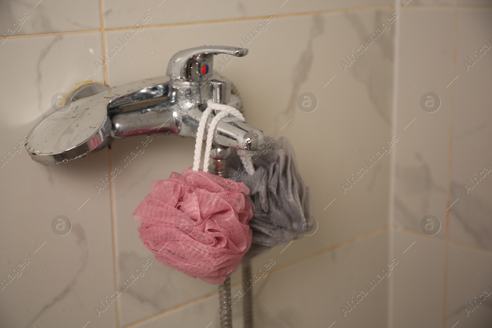 Photo of Colorful shower puffs hanging on faucet in bathroom. Space for text