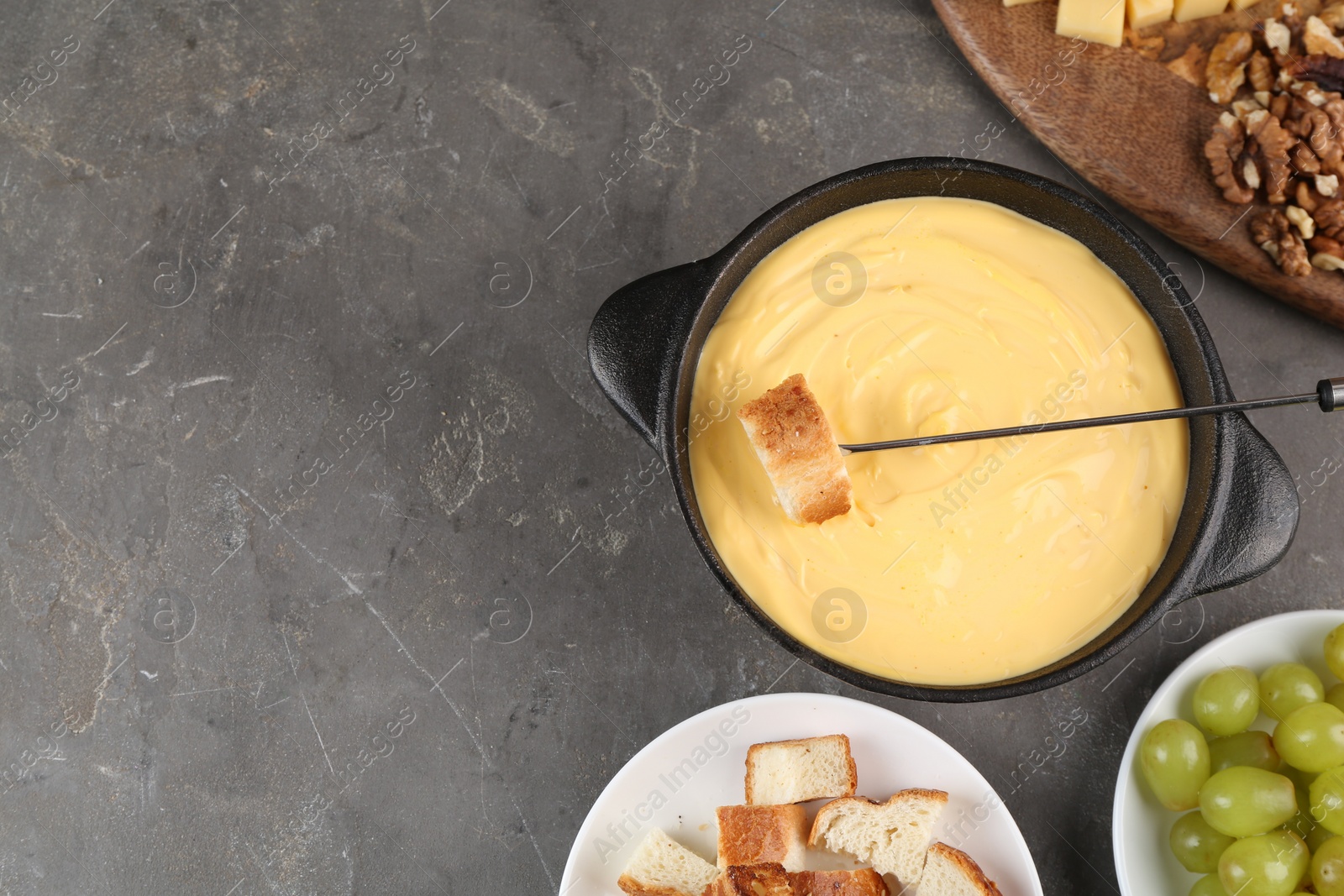 Photo of Fondue pot with tasty melted cheese, fork and different snacks on grey table, flat lay. Space for text