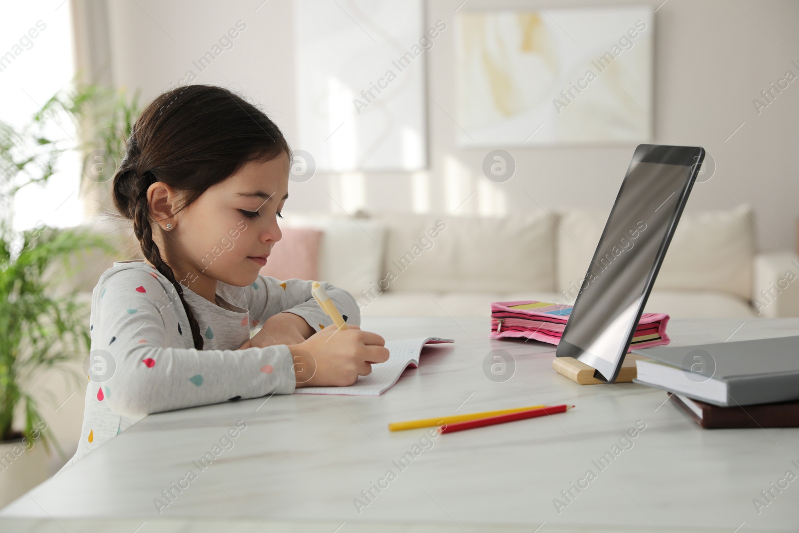 Photo of Little girl doing homework with modern tablet at home