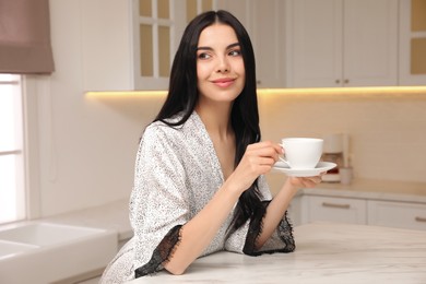 Photo of Pretty young woman wearing beautiful silk robe with cup of coffee in kitchen