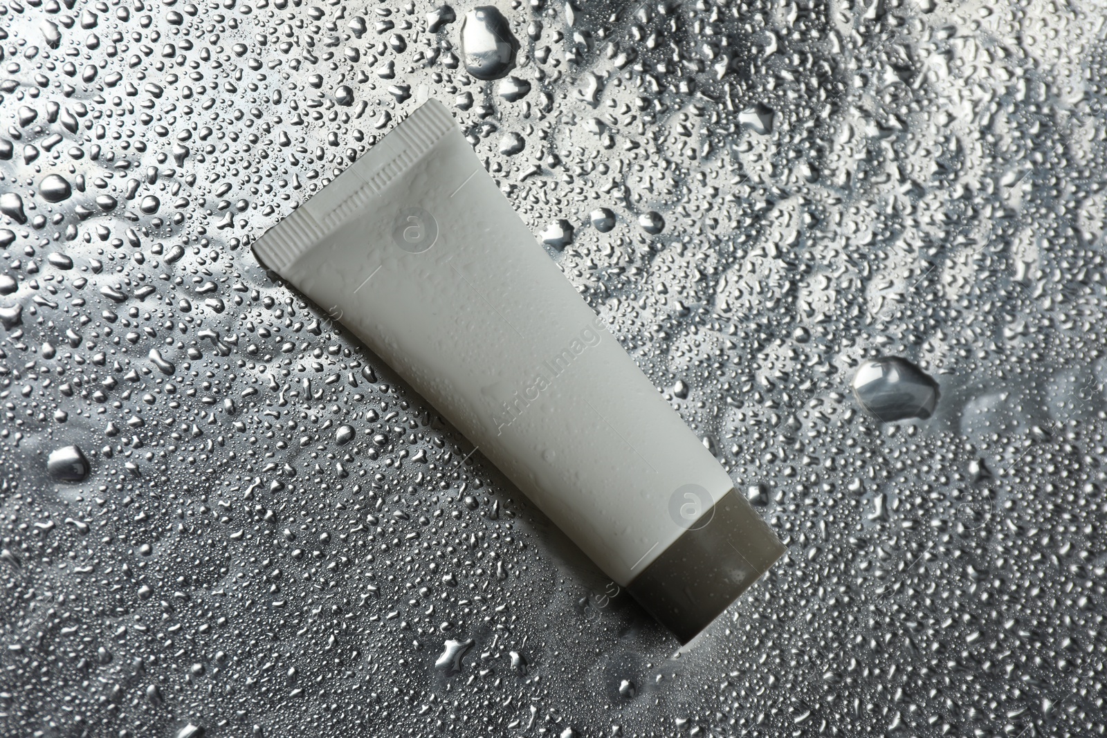 Photo of Moisturizing cream in tube on silver background with water drops, top view