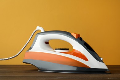 Photo of One modern iron on wooden table against orange background. Home appliance