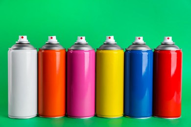 Photo of Colorful cans of spray paints on green background