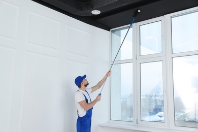 Photo of Worker in uniform painting ceiling with roller indoors