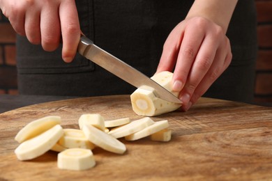 Photo of Woman cutting delicious fresh ripe parsnip at wooden board, closeup