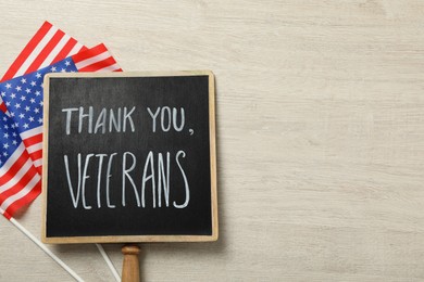 Photo of Sign with phrase Thank You, Veterans and American flags on white wooden table, flat lay. Space for text