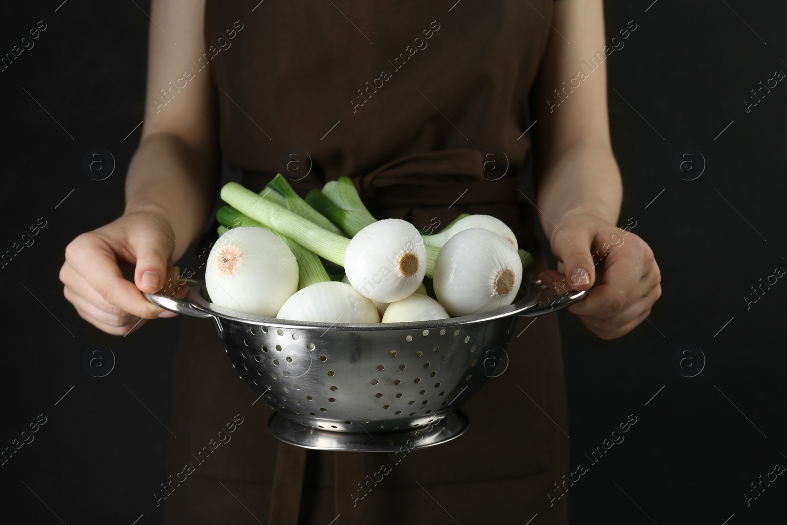 Photo of Woman holding colander with green spring onions on black background, closeup