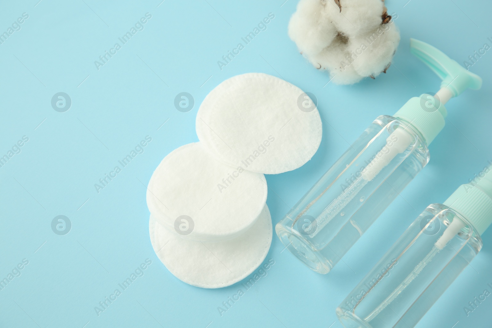 Photo of Cosmetic products, cotton pads and flower on light blue background, above view. Space for text