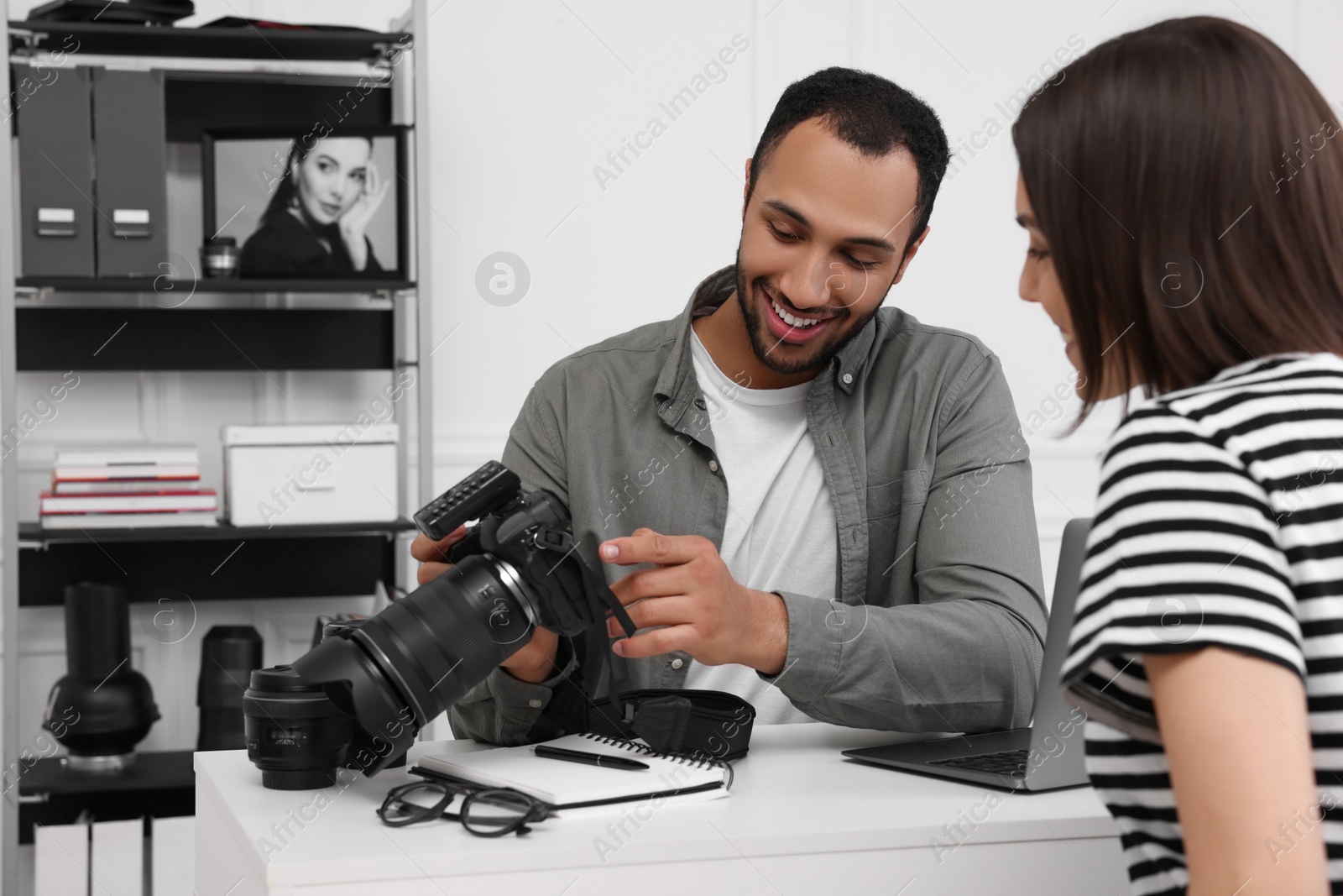 Photo of Young professional photographer showing camera to woman in modern photo studio