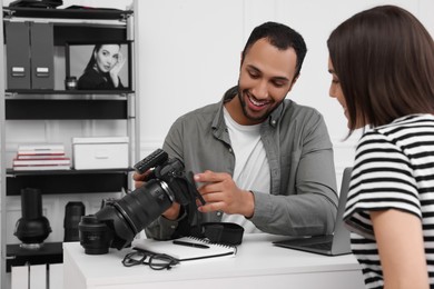 Young professional photographer showing camera to woman in modern photo studio
