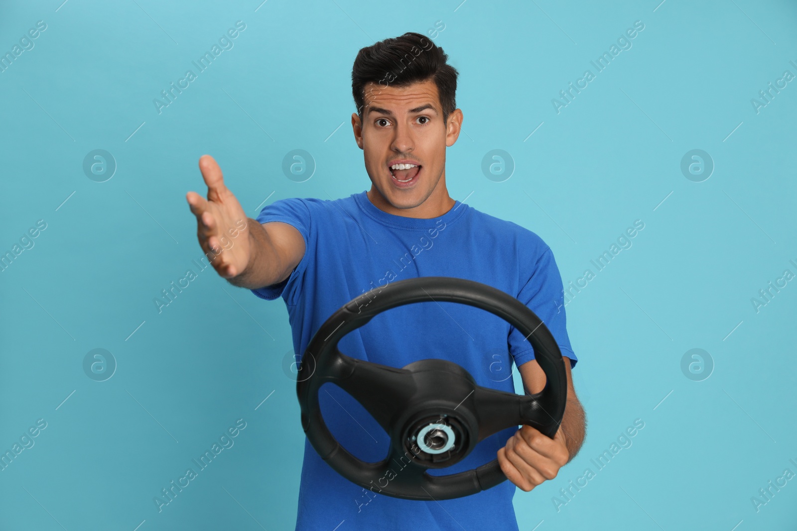 Photo of Emotional man with steering wheel on light blue background