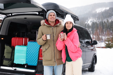 Happy couple with drinks near car on snowy road. Winter vacation