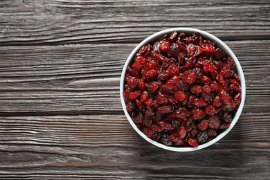 Photo of Bowl with cranberries on wooden background, top view with space for text. Dried fruit as healthy snack