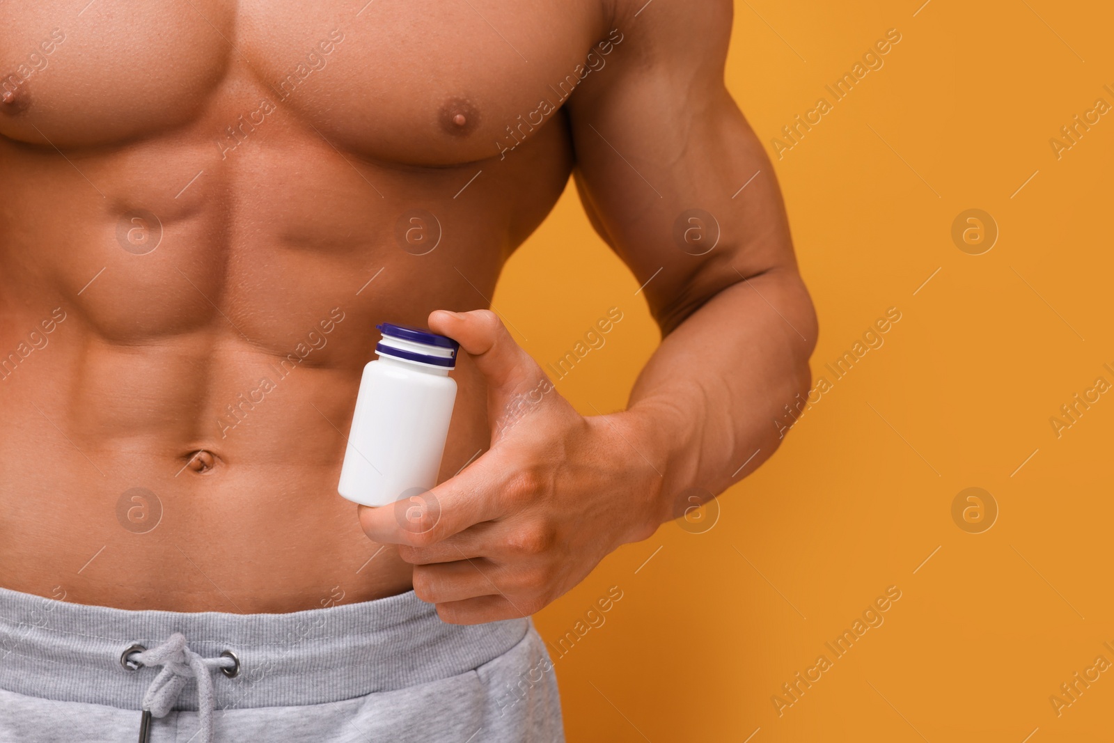 Photo of Weight loss. Athletic man with bottle of supplements on orange background, closeup. Space for text