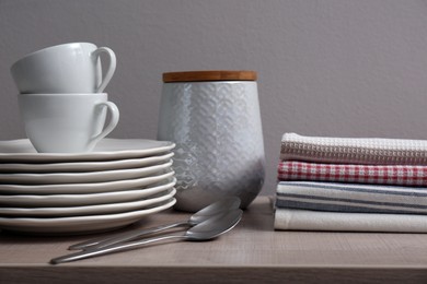 Photo of Stack of soft kitchen towels and dishware on wooden table against grey background