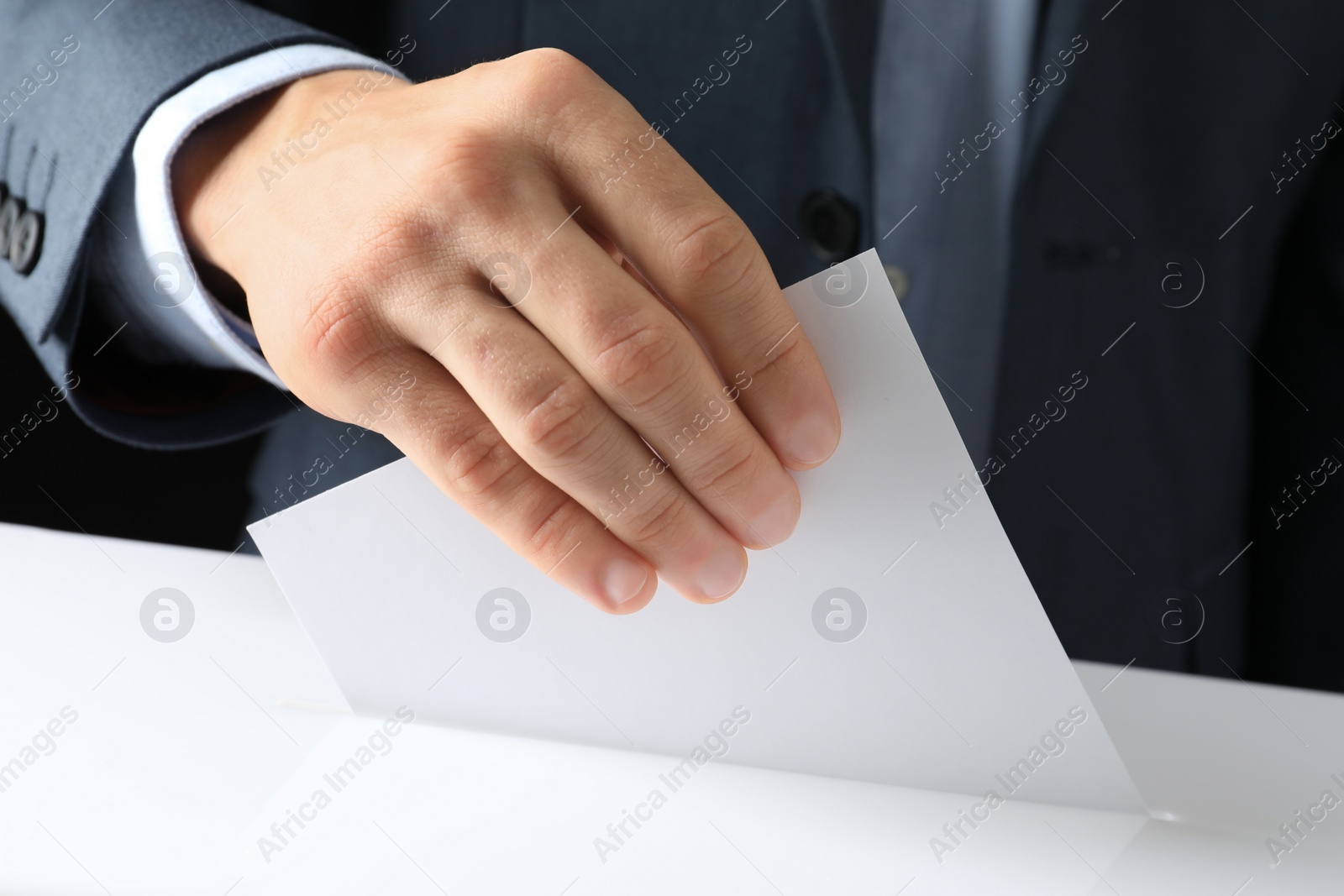 Photo of Man putting his vote into ballot box on black background, closeup