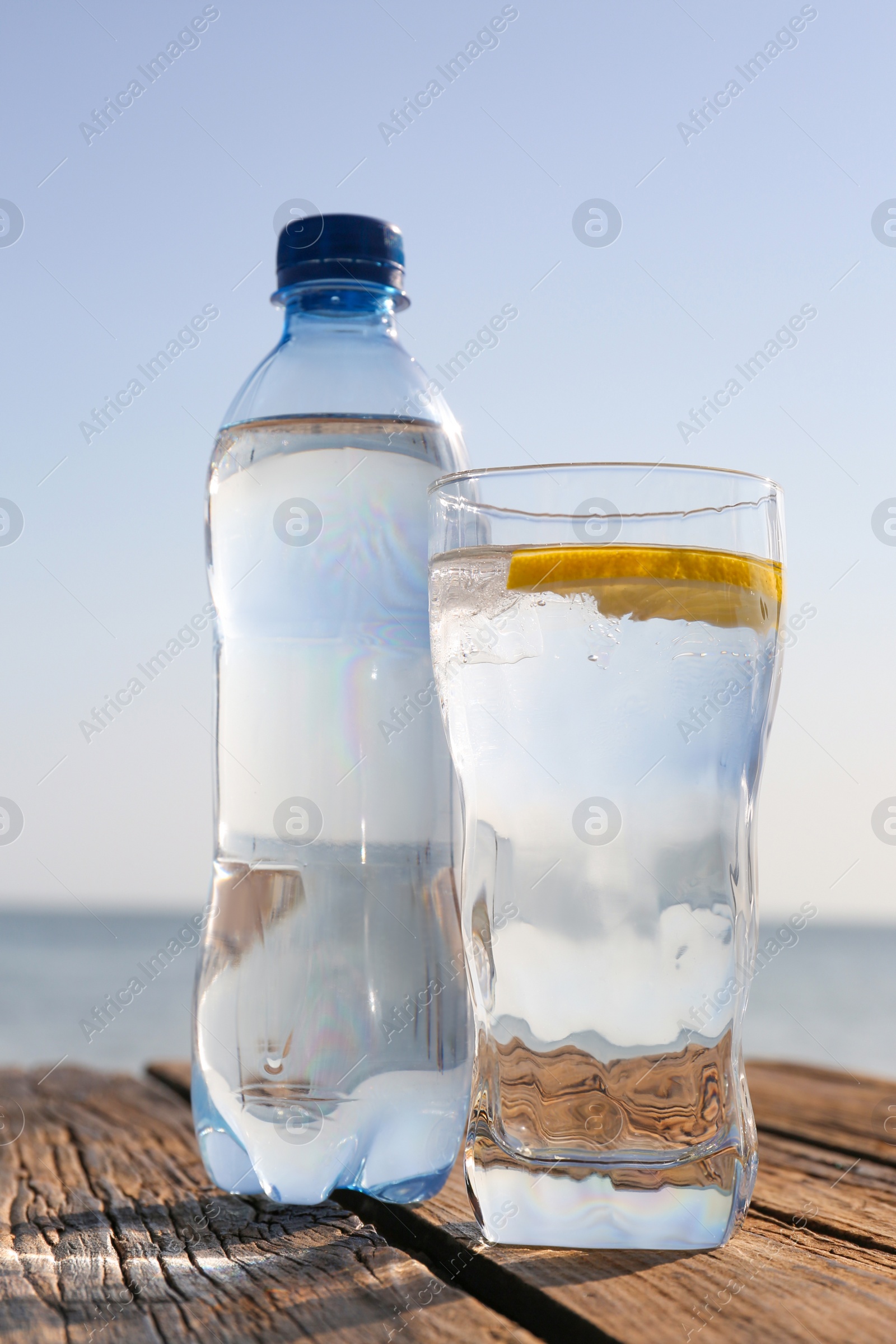 Photo of Wooden table with glass and bottle of refreshing drink on hot summer day outdoors