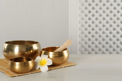 Golden singing bowls, mallet and flower on white wooden table, space for text