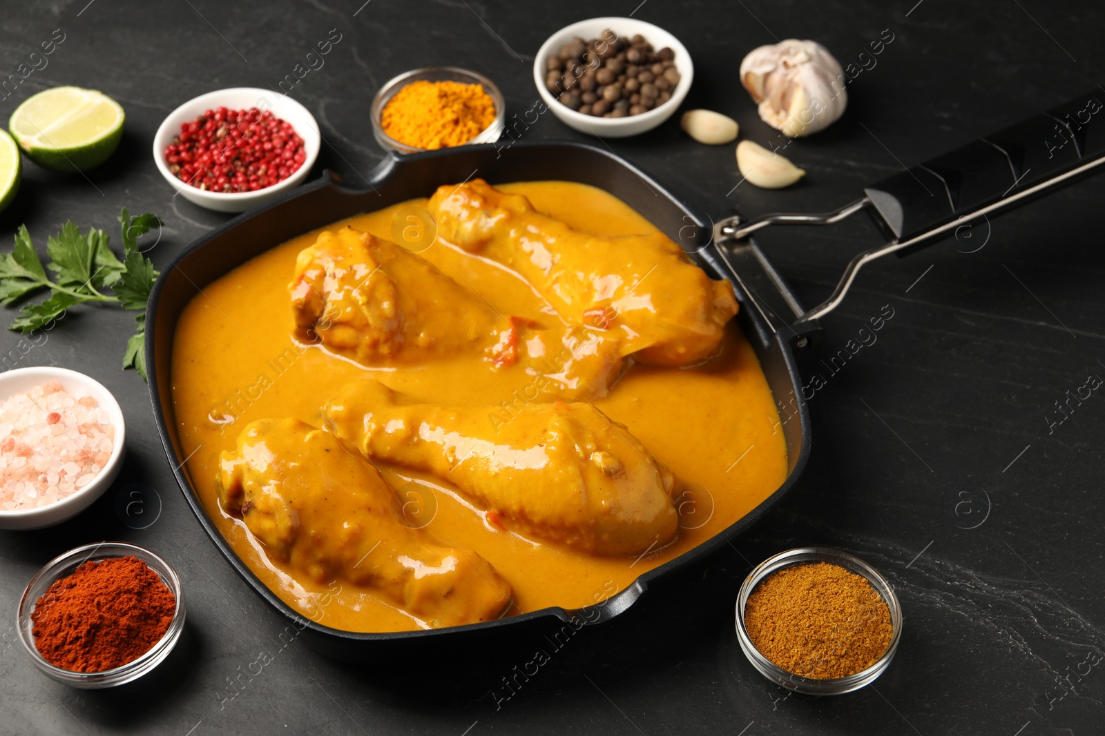 Photo of Tasty chicken curry and ingredients on black textured table