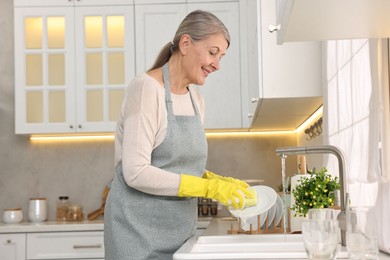 Happy housewife washing plate in kitchen sink