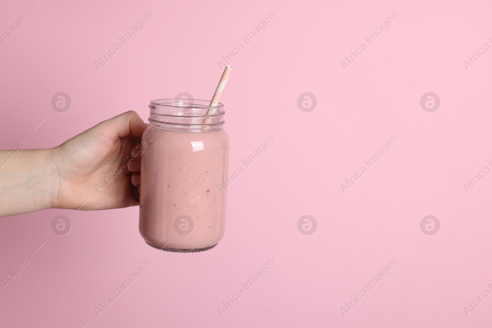 Photo of Woman holding mason jar of tasty smoothie on pink background, closeup. Space for text