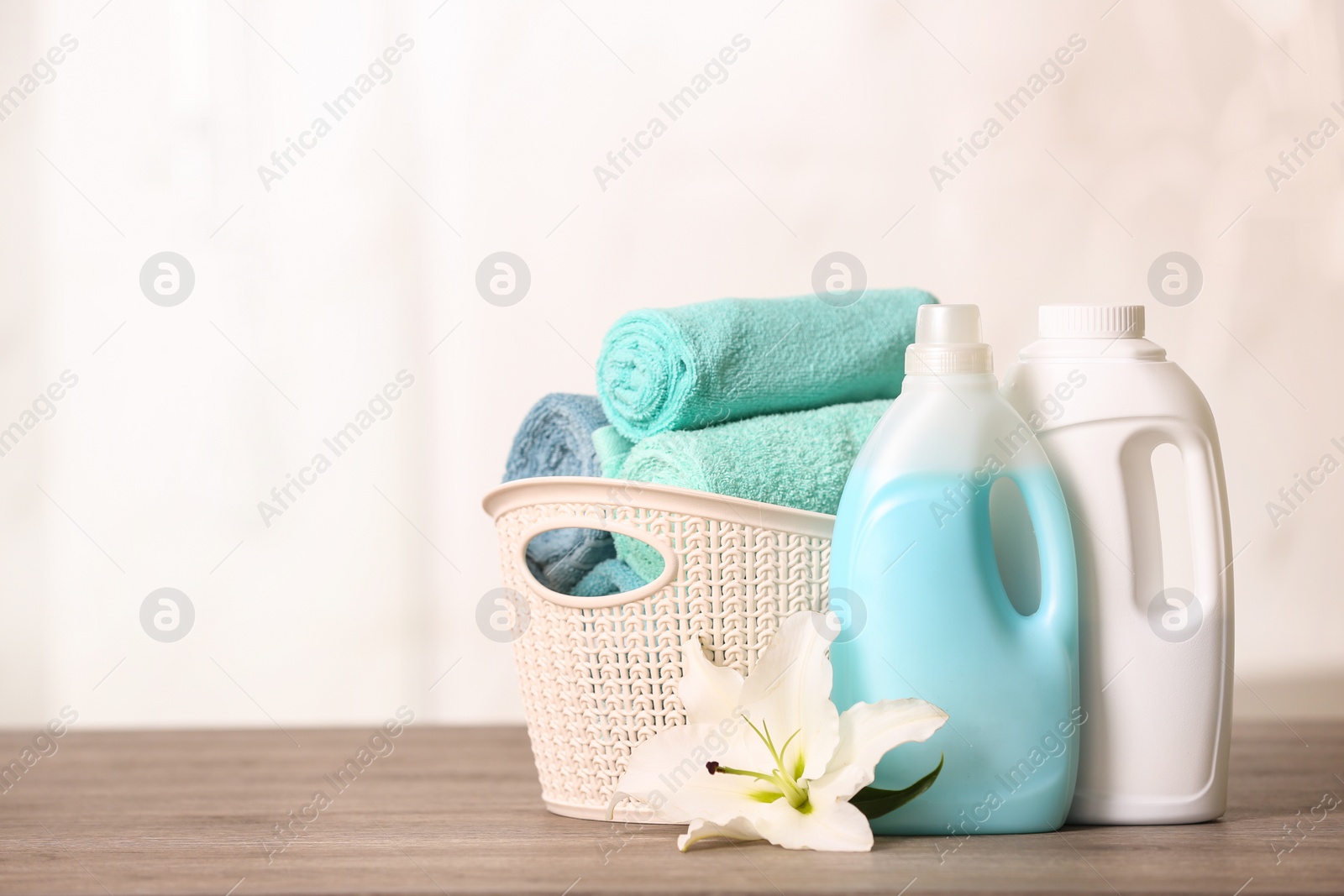 Photo of Clean towels in basket with lily and detergents on table. Space for text