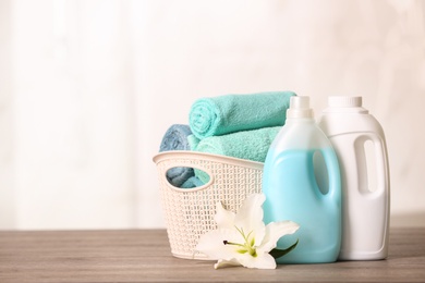 Photo of Clean towels in basket with lily and detergents on table. Space for text