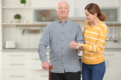 Photo of Elderly man with female caregiver in kitchen. Space for text