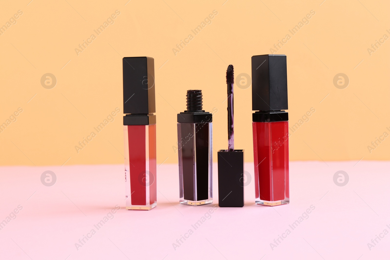 Photo of Different lip glosses and applicator on color background