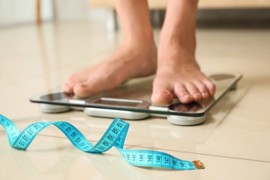 Photo of Tape in front of woman standing on floor scales indoors. Overweight problem