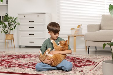 Photo of Little boy with cute ginger cat on carpet at home