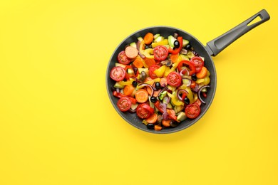 Photo of Mix of tasty vegetables in pan on yellow background, top view. Space for text