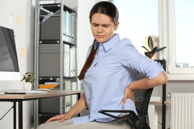 Young woman suffering from back pain while sitting in office. Symptom of scoliosis
