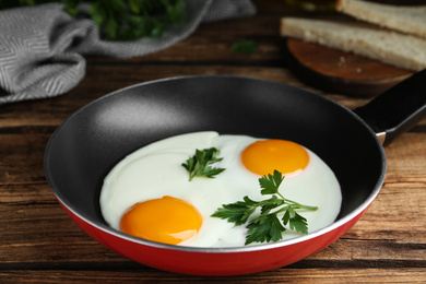 Photo of Tasty cooked chicken eggs with parsley in frying pan on wooden table, closeup