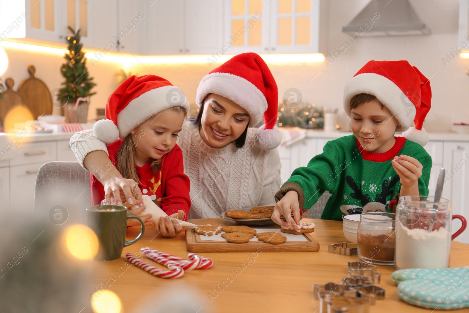Photo of Mother and her cute little children decorating tasty Christmas cookies at table in kitchen