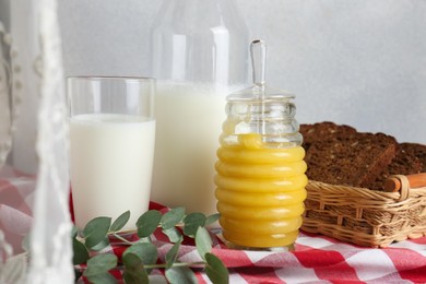 Photo of Jar with tasty honey, milk and bread on checkered cloth