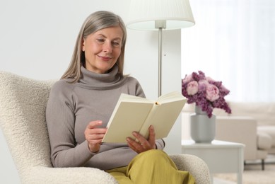 Photo of Beautiful senior woman reading book in armchair at home