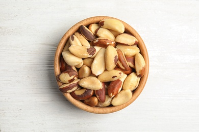 Photo of Bowl with tasty Brazil nuts on white wooden background, top view