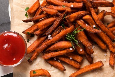 Photo of Delicious sweet potato fries and sauce on parchment paper, top view