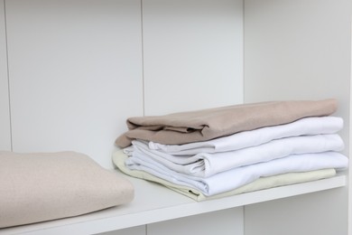 Photo of Stack of different folded shirts on white shelf. Organizing clothes