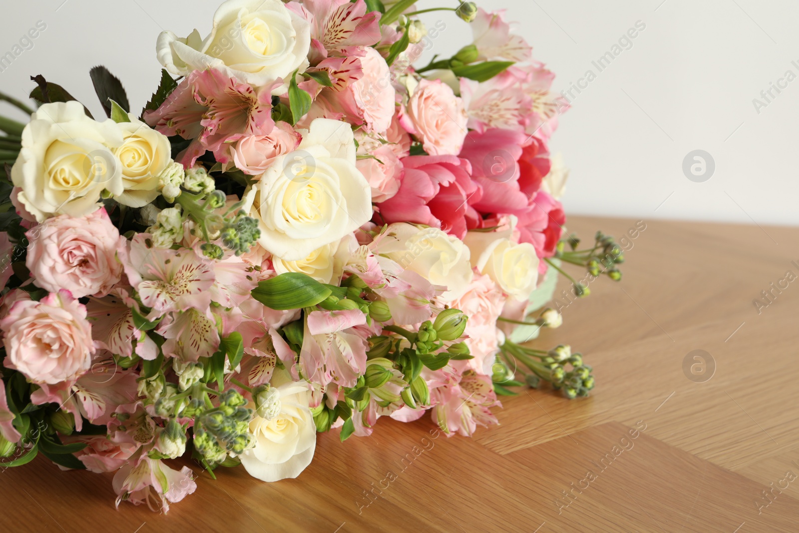 Photo of Beautiful bouquet of fresh flowers on wooden table near white wall, closeup. Space for text