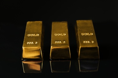 Photo of Precious shiny gold bars on black background