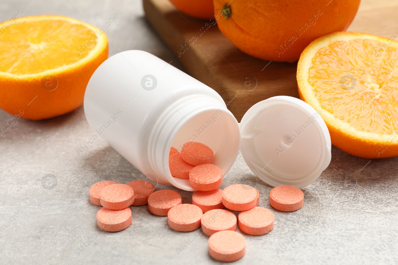 Photo of Dietary supplements. Overturned bottle, pills and oranges on grey table