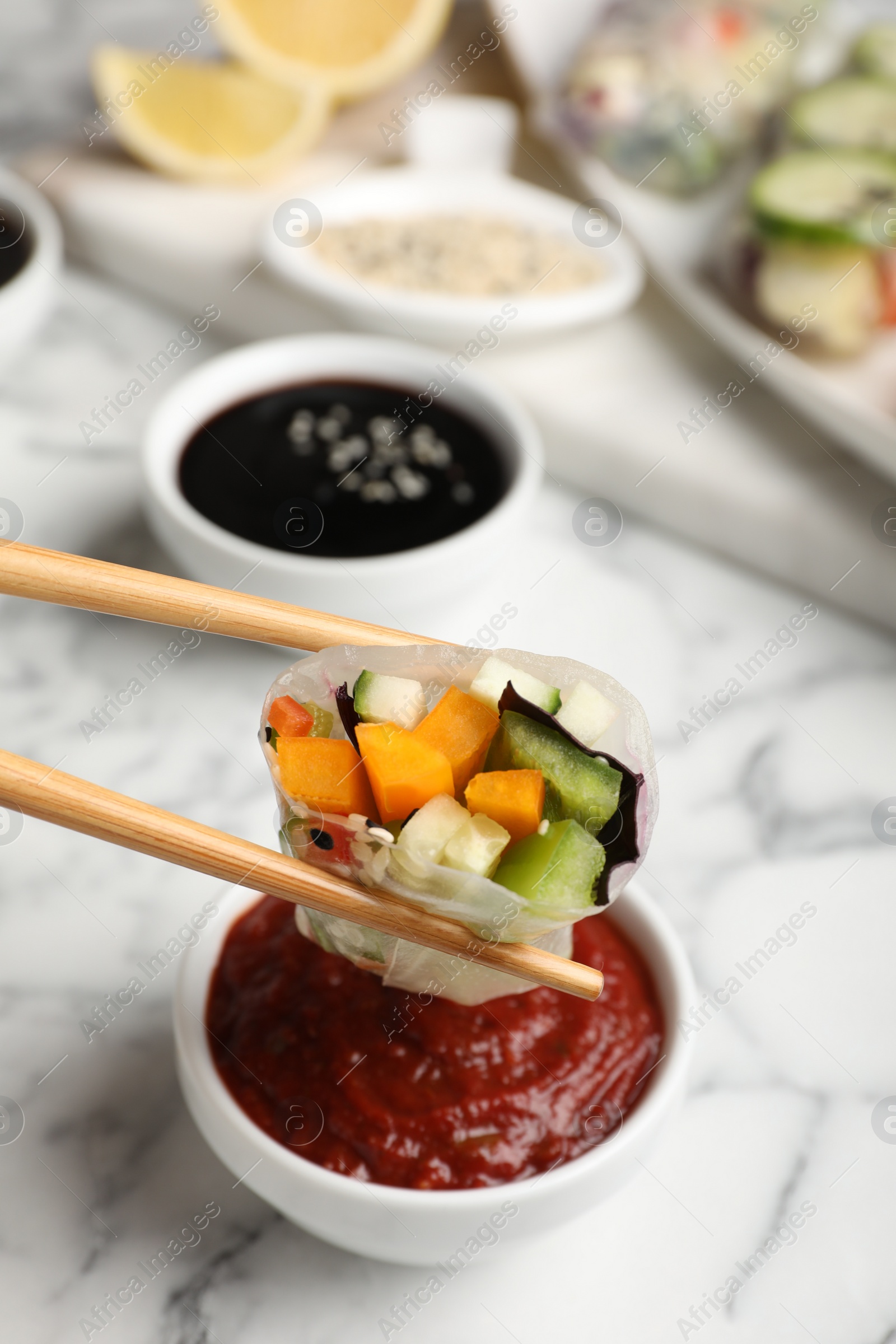 Photo of Dipping delicious roll wrapped in rice paper into sauce at white marble table