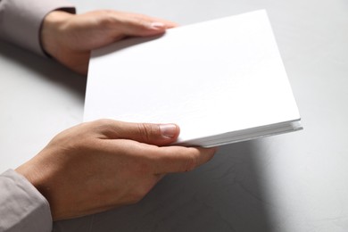 Photo of Man holding blank book at light grey table, closeup. Mockup for design