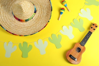 Mexican sombrero hat, maracas, ukulele and garland on yellow background, flat lay