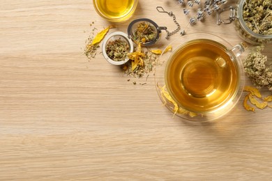 Photo of Freshly brewed tea and dried herbs on wooden table, flat lay. Space for text