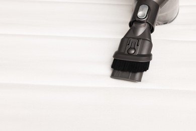 Photo of Modern vacuum cleaner on white mattress, closeup. Space for text